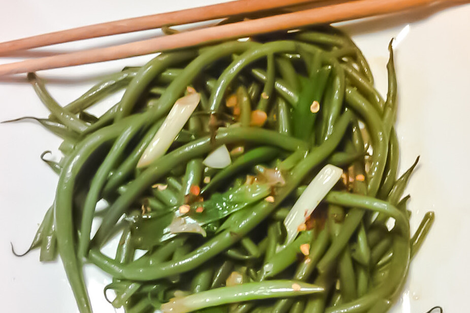 Szechuan green bean salad served on a white plate with chopsticks