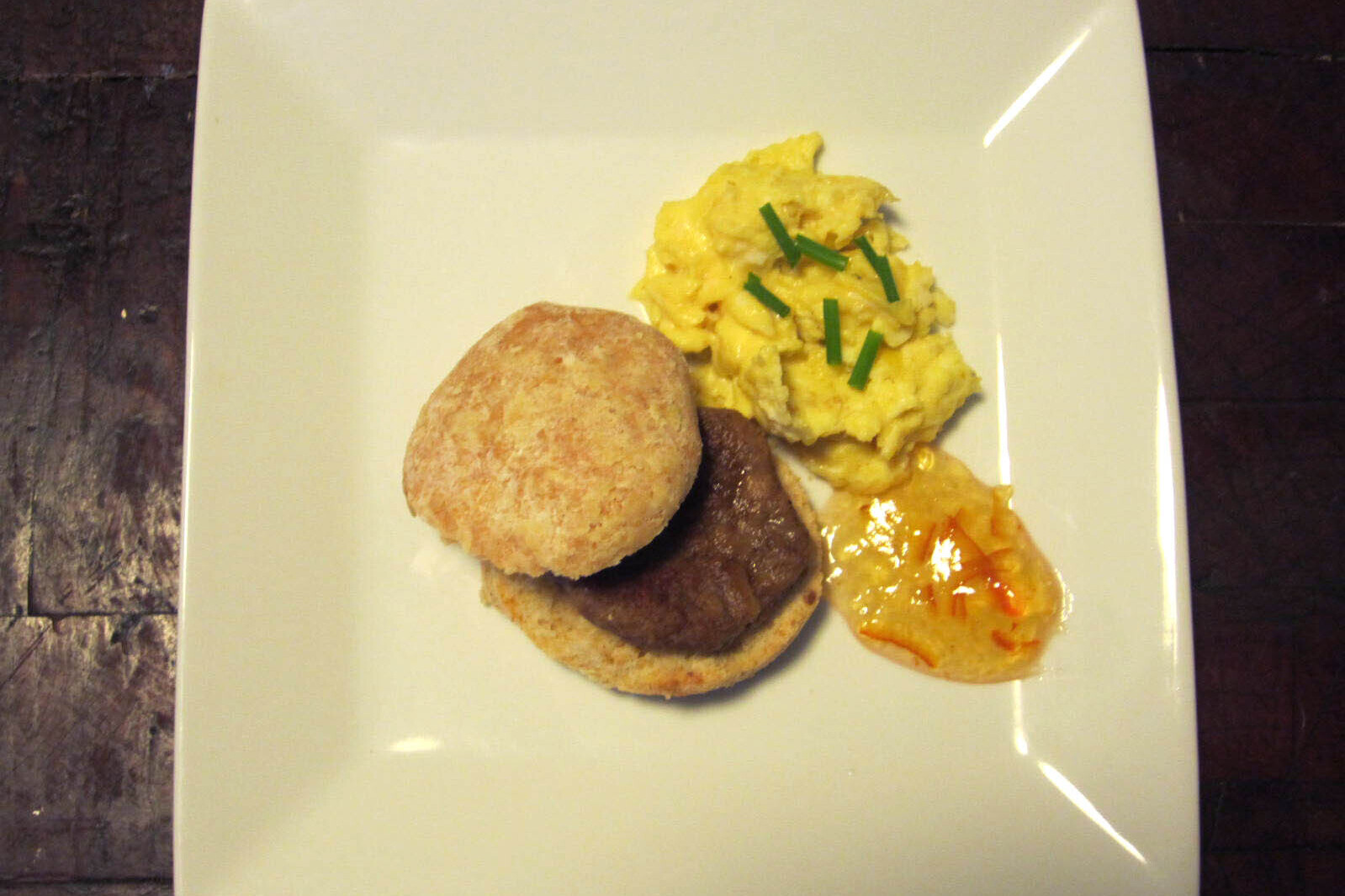 A plate with a vegetarian sausage breakfast sandwich with eggs and jam on the side