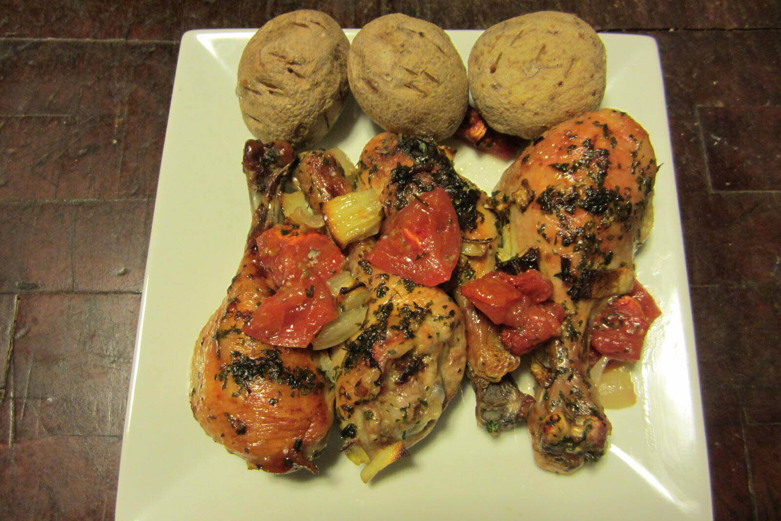 Chicken topped with tomato and onion with baked potatoes on the side