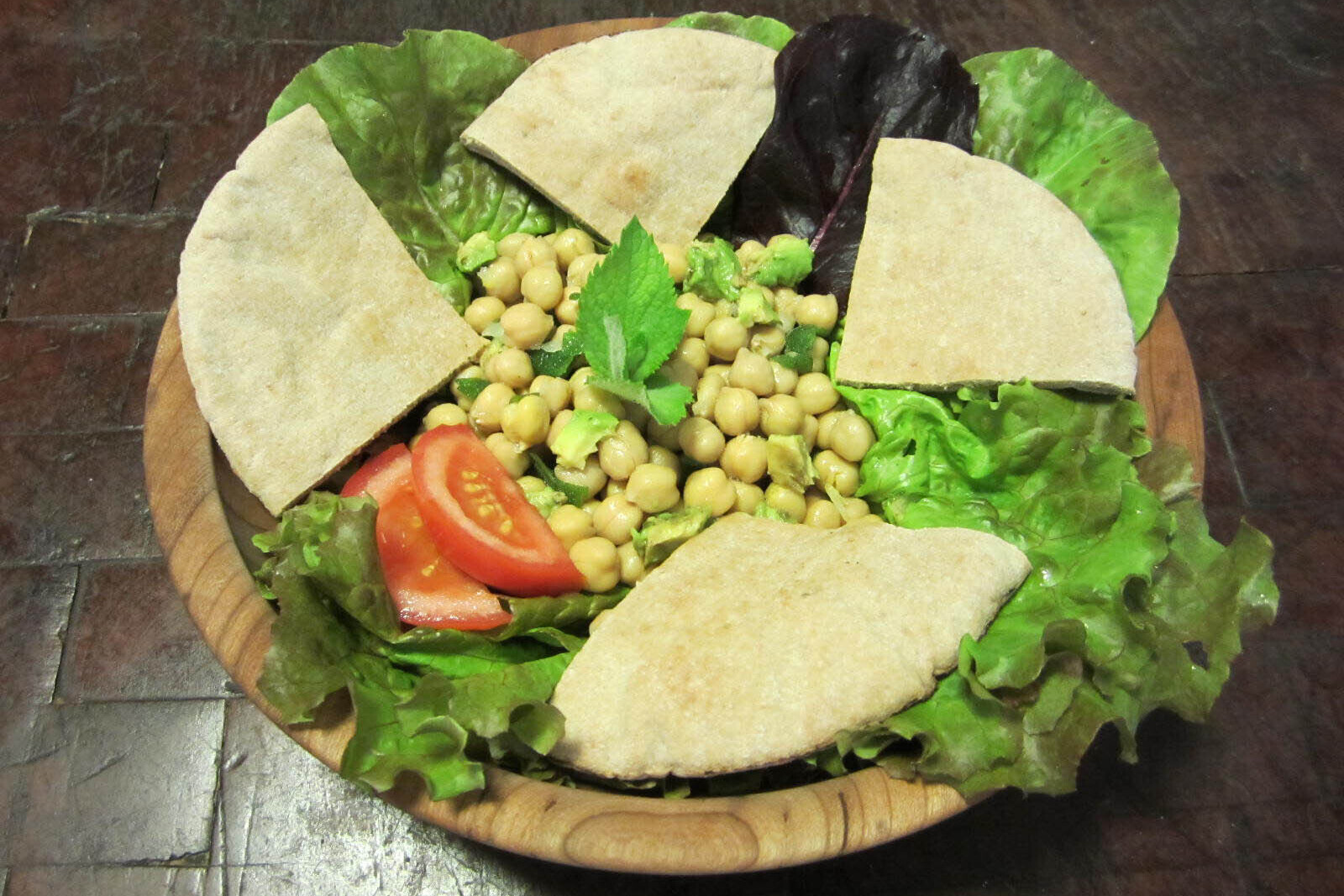Bed of lettuce with chickpeas, sliced tomato, and pita bread