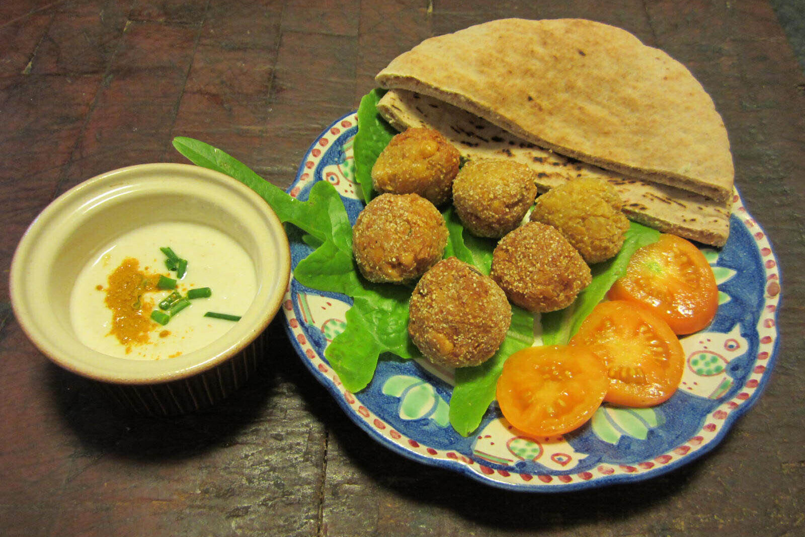 Falafel on a bed of lettuce, with tomatoes pita bread, and a side of tahini/lemon/yogurt sauce