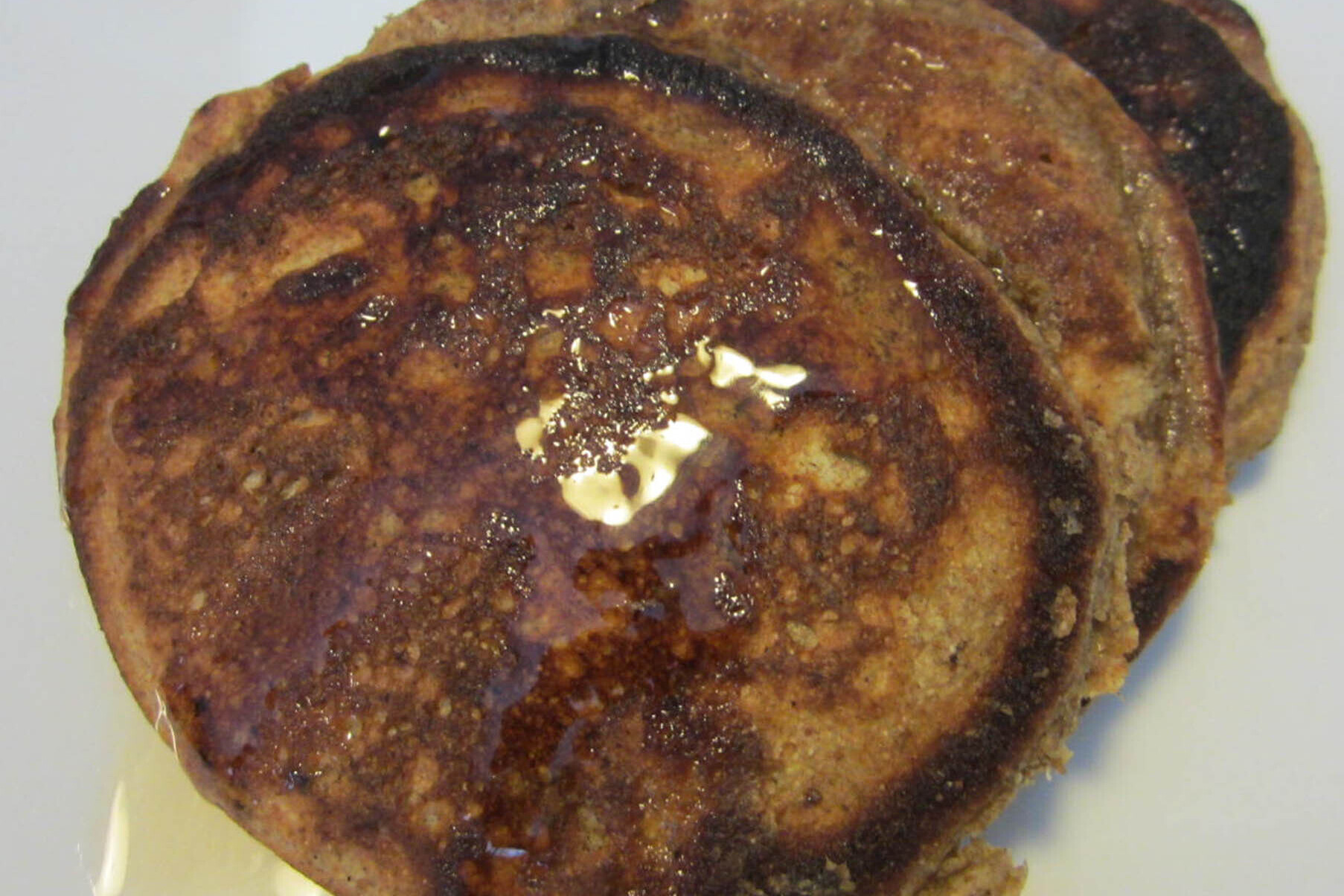 Three peanut coconut pancakes with maple syrup on a white plate