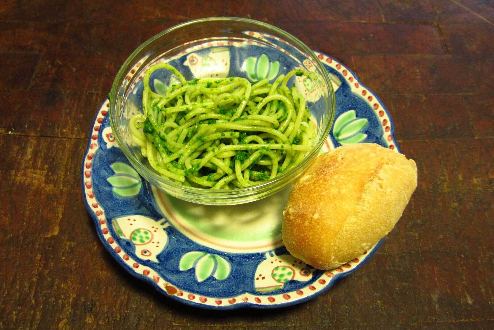Bowl of pasta with spinach pesto and a roll on the side