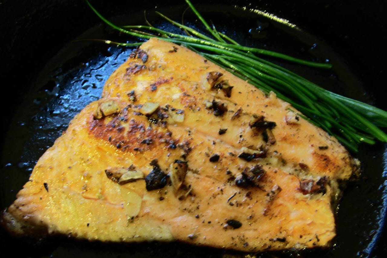 cooked salmon with a side of chives on a cast iron pan