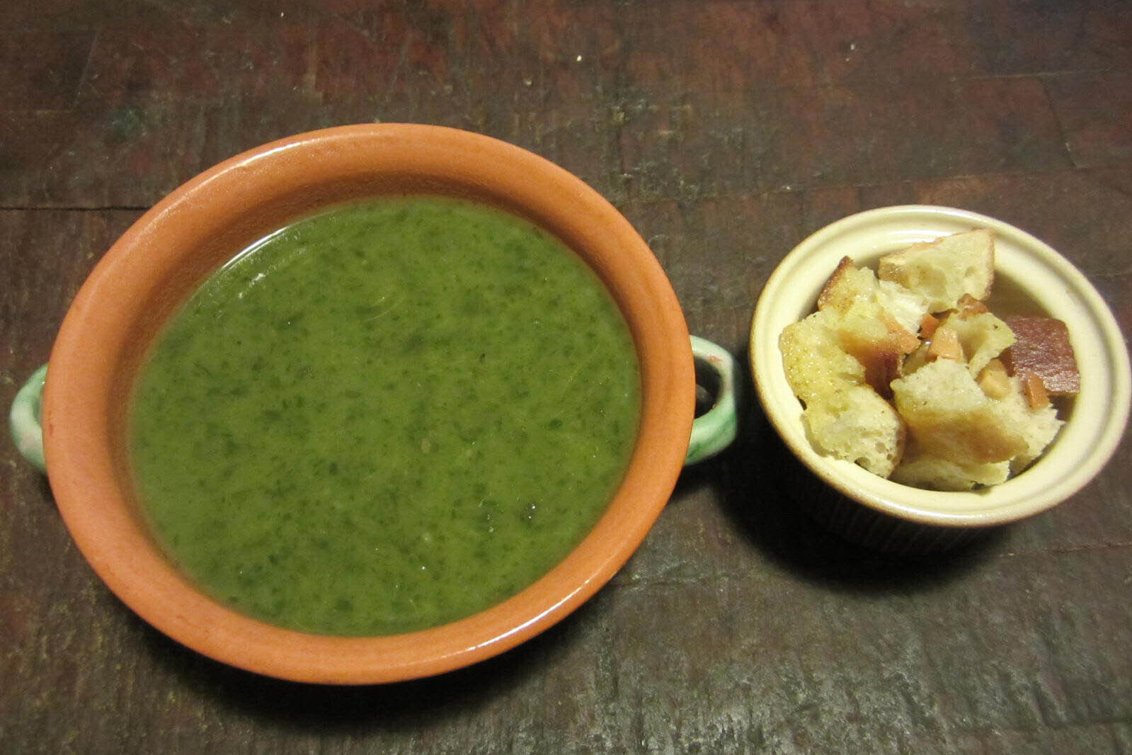 Bowl of leafy greens soup with garlic croutons on the side