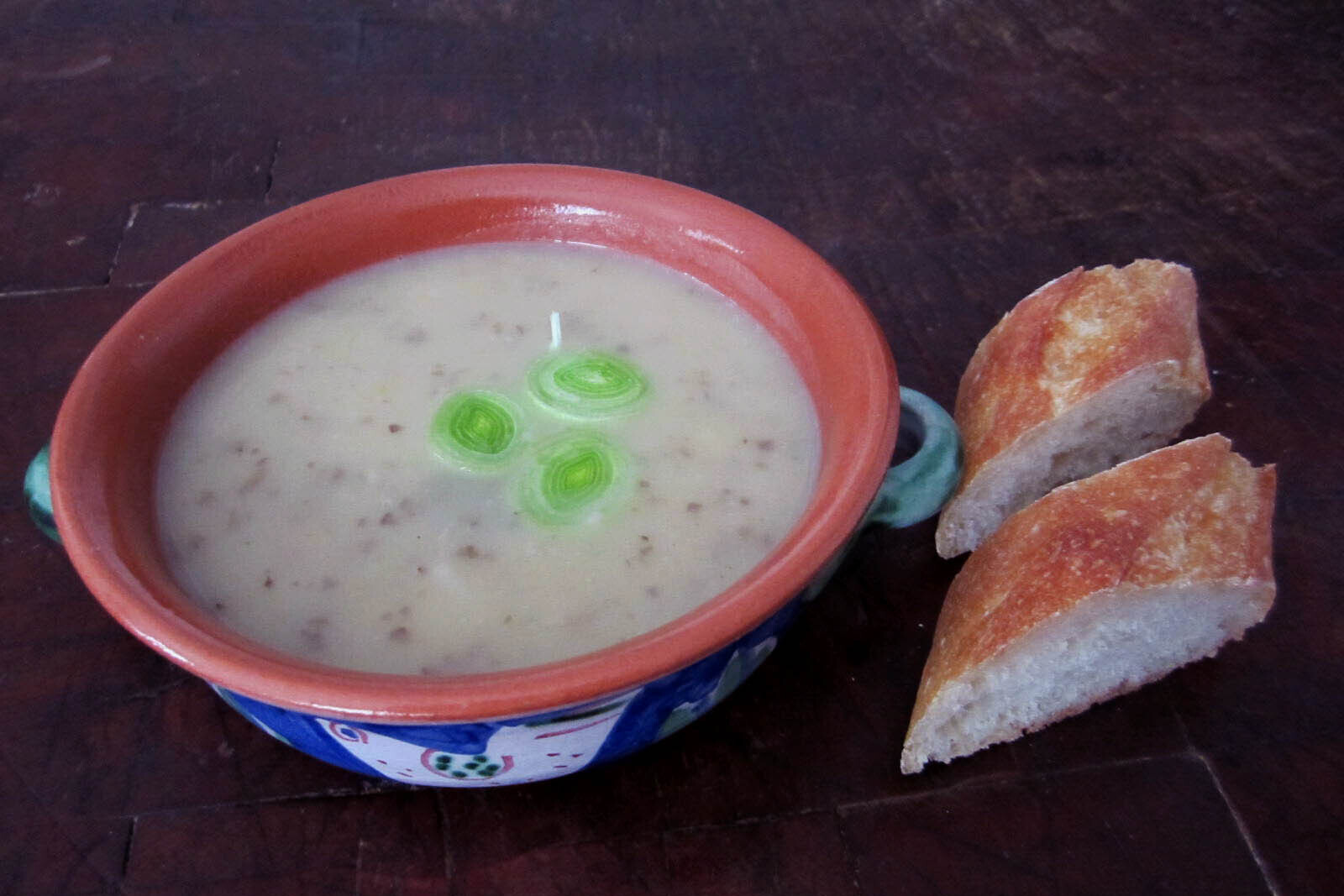 Bowl of potato leek soup with two slices of a baguette on the side