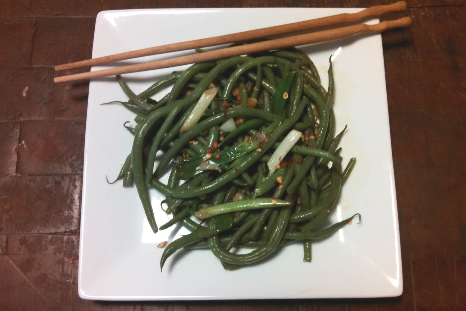 Szechuan green bean salad served on a white plate with chopsticks