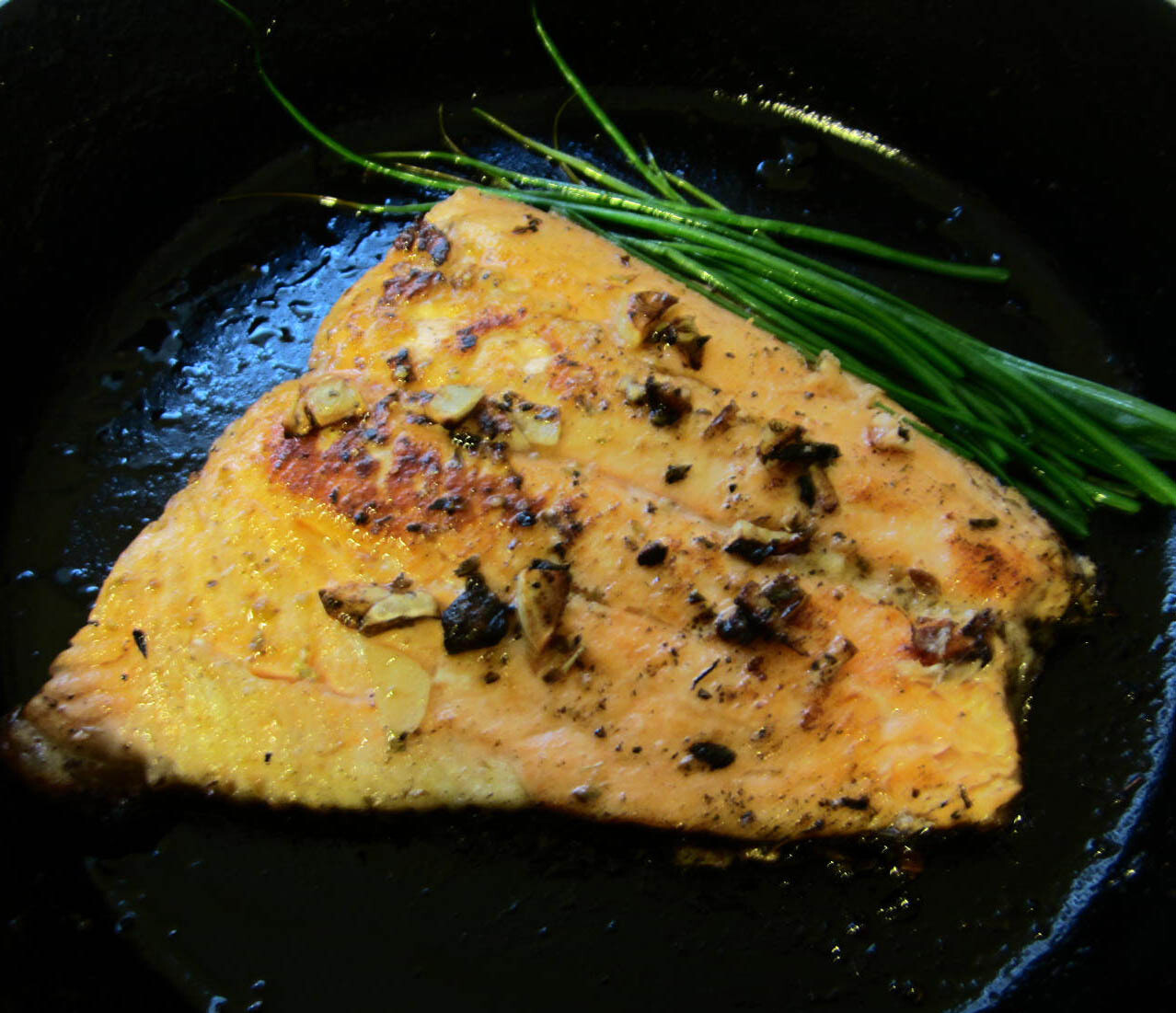 cooked salmon with a side of chives on a cast iron pan