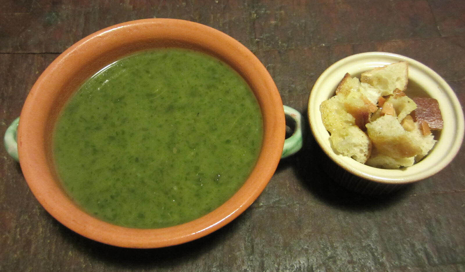 Bowl of leafy greens soup with garlic croutons on the side
