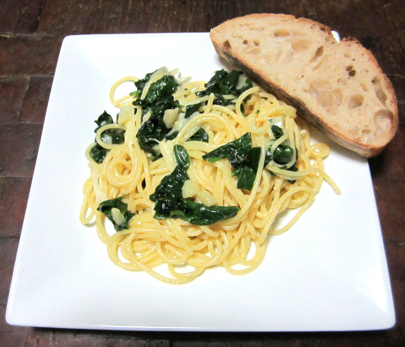 Spaghetti topped with spinach and cheese with a slice of bread on the side