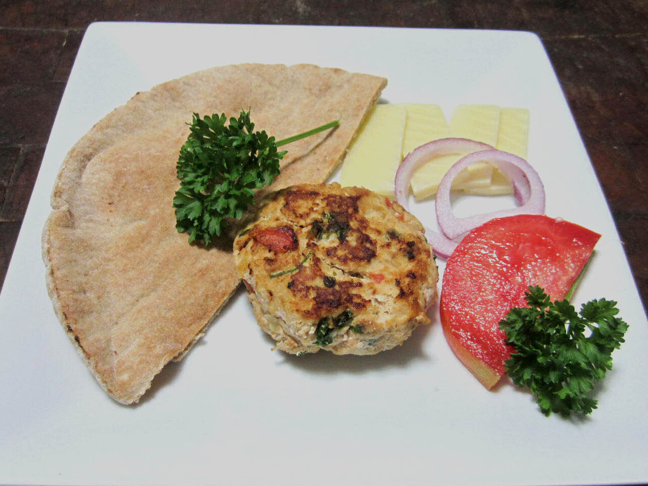 Tomato parsley burger with pita bread, parsley, cheese, red onion, and a slice of tomato