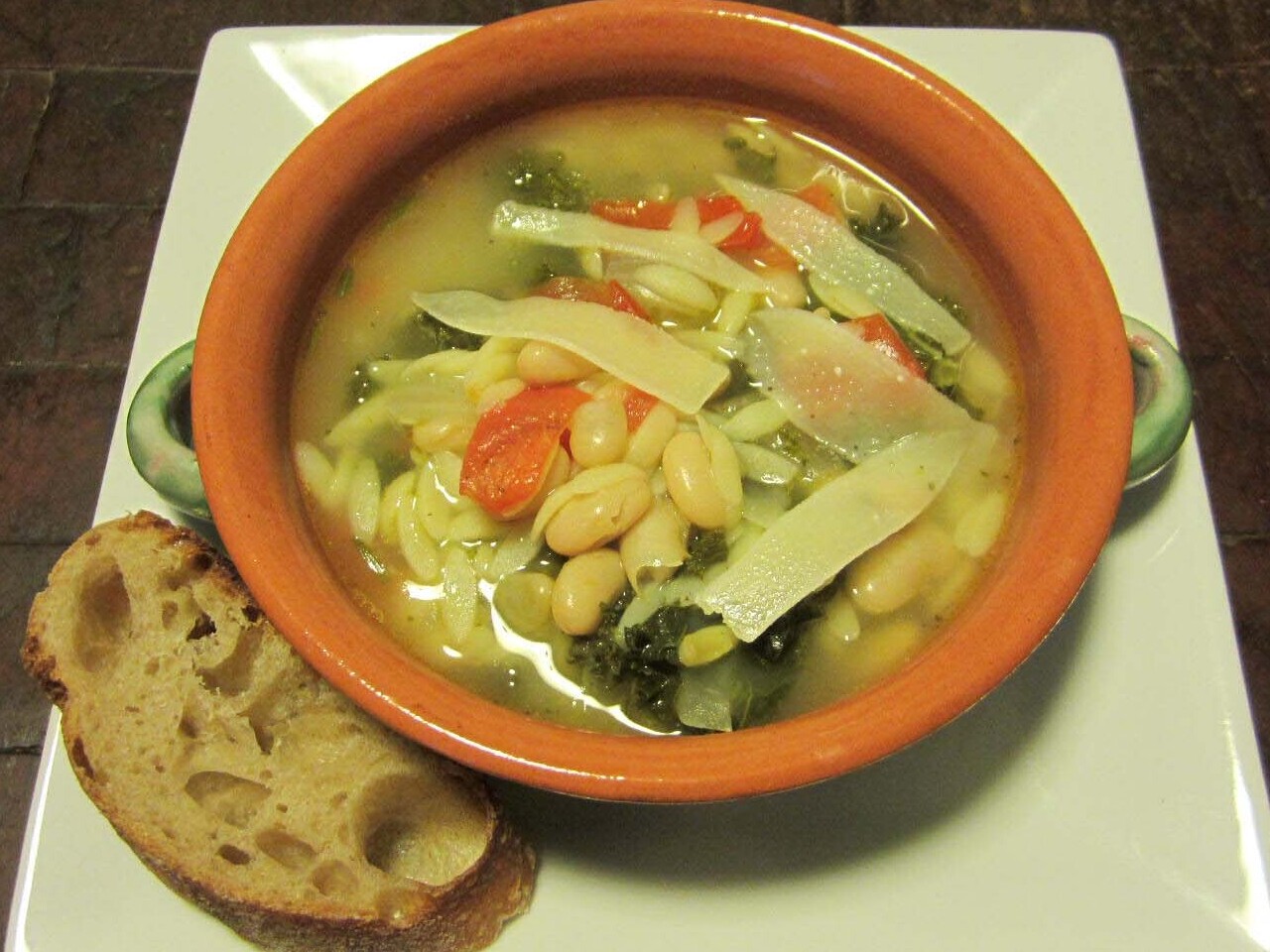 Bowl of kale, bean and orzo soup with a slice of bread on the side