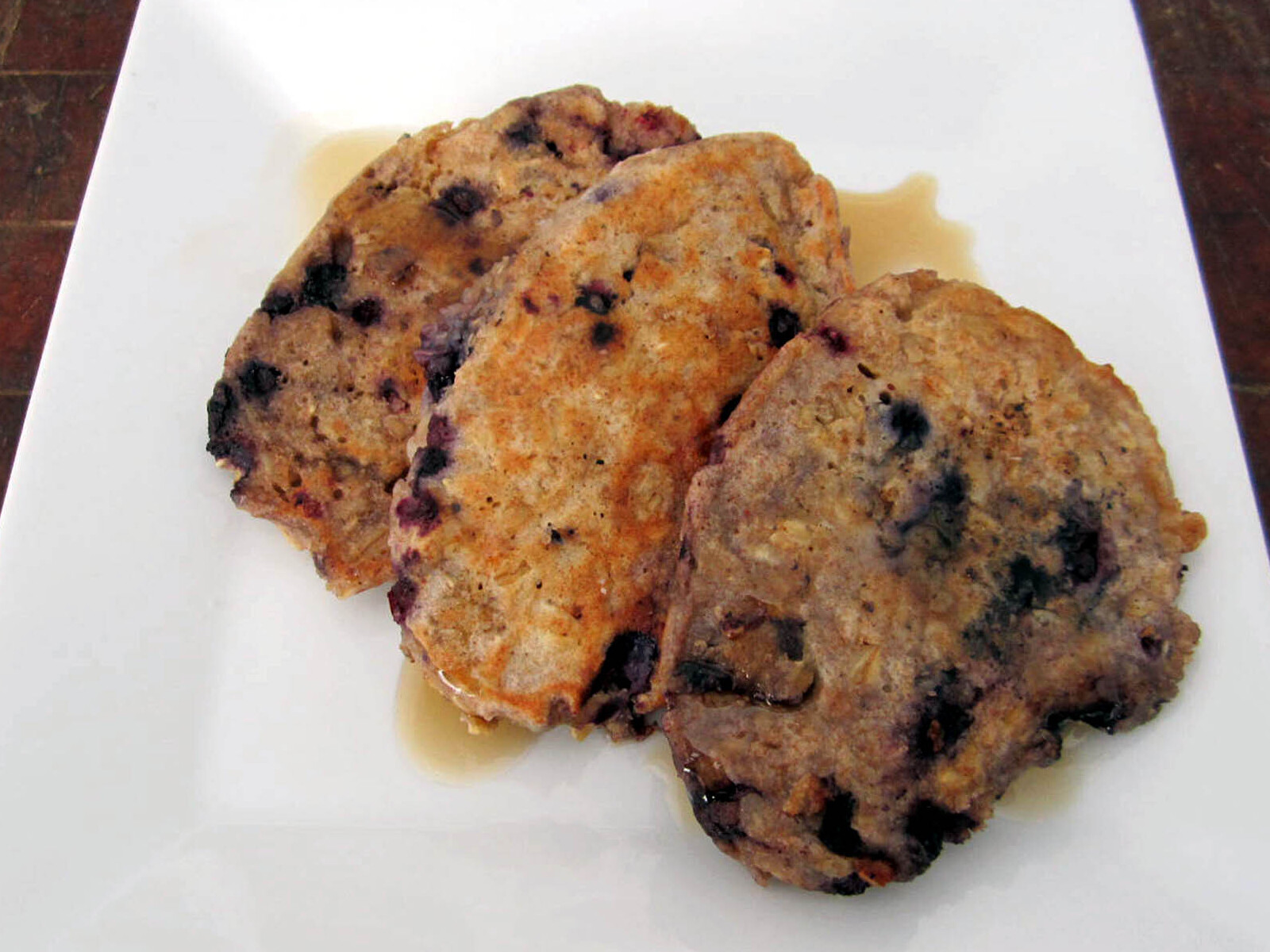 Three oat blueberry pancakes with maple syrup on a white plate