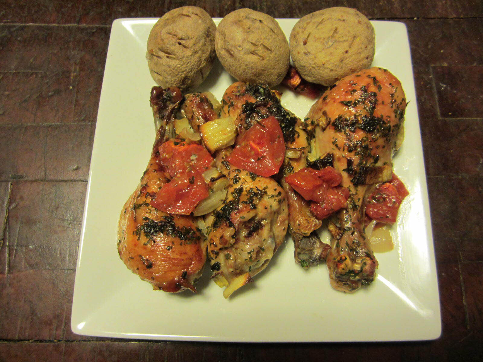 Chicken topped with tomato and onion with baked potatoes on the side