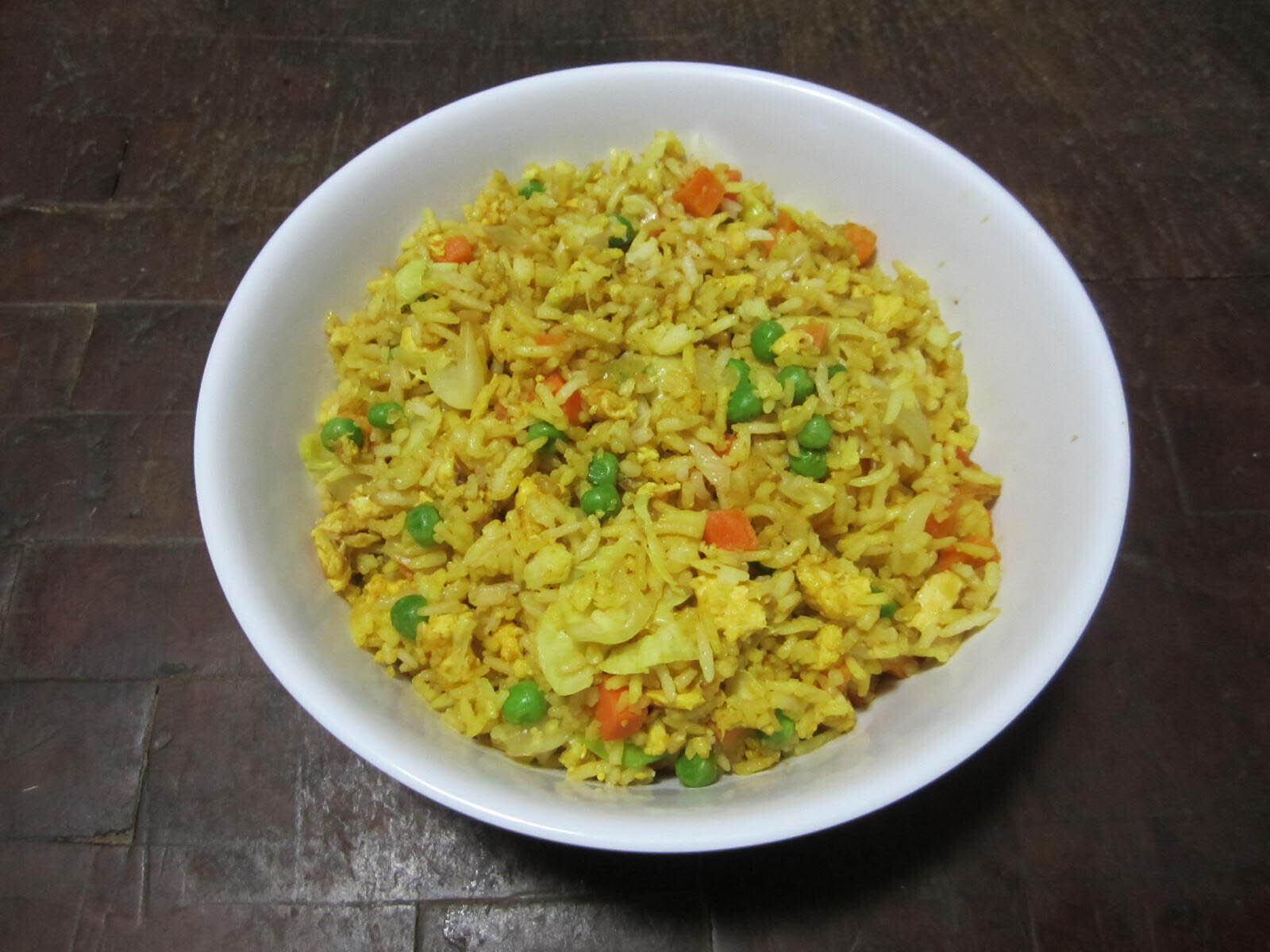 A bowl of yellow fried rice with peas, carrots, and onion