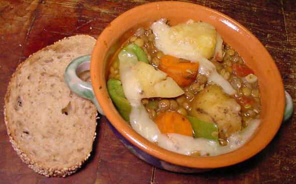 Bowl of lentil and potato stew and a slice of bread on the side