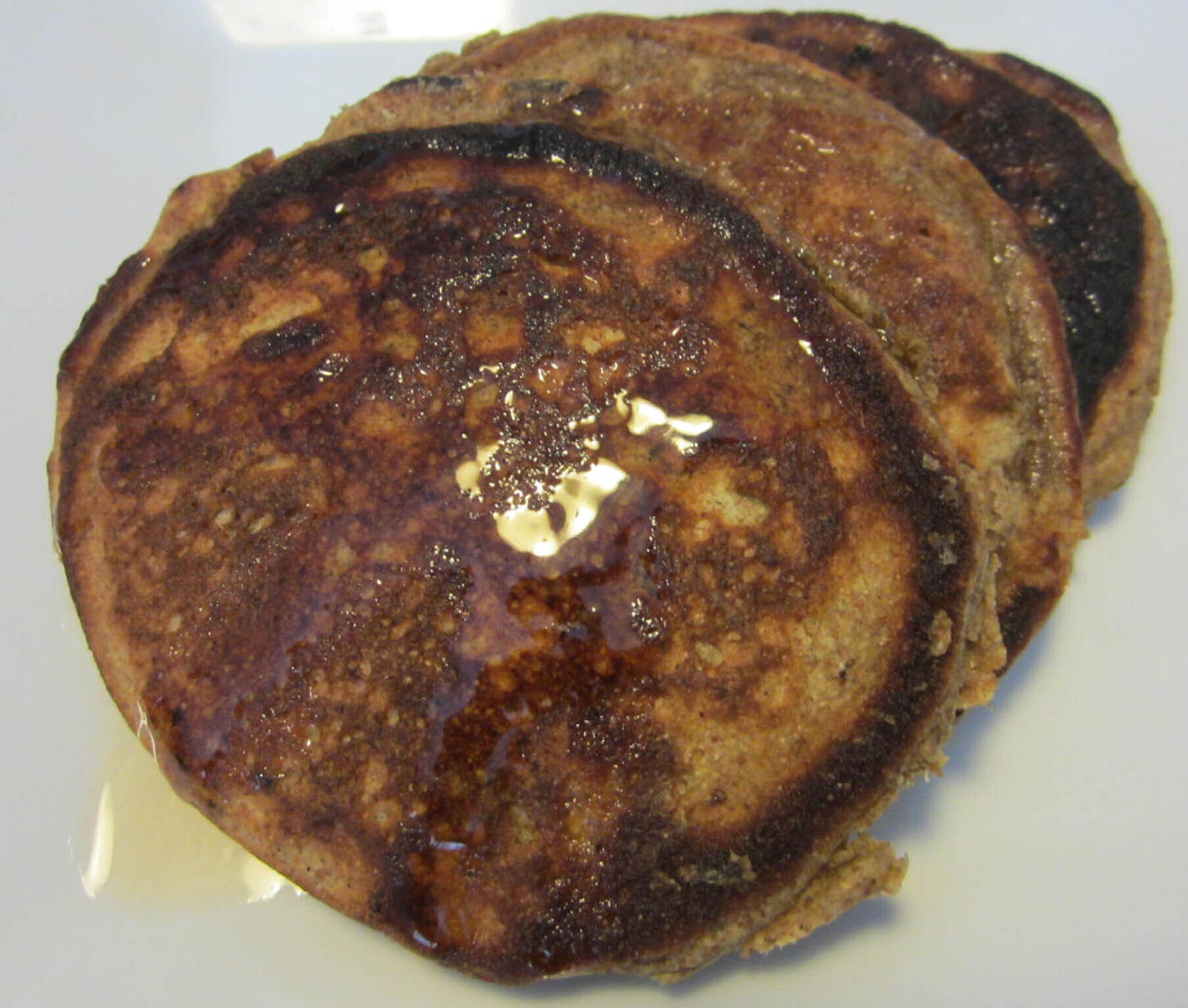 Three peanut coconut pancakes with maple syrup on a white plate
