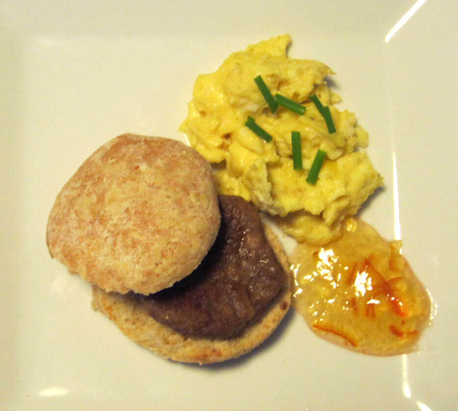 A plate with a vegetarian sausage breakfast sandwich with eggs and jam on the side