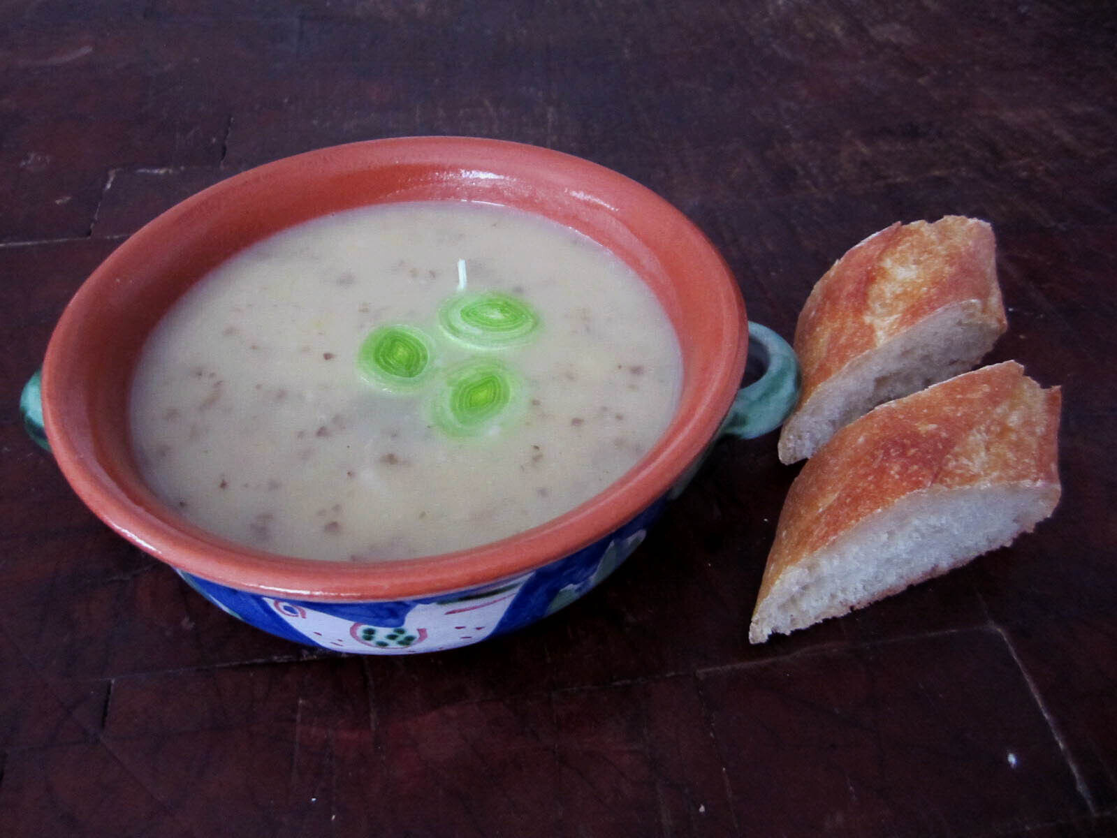 Bowl of potato leek soup with two slices of a baguette on the side