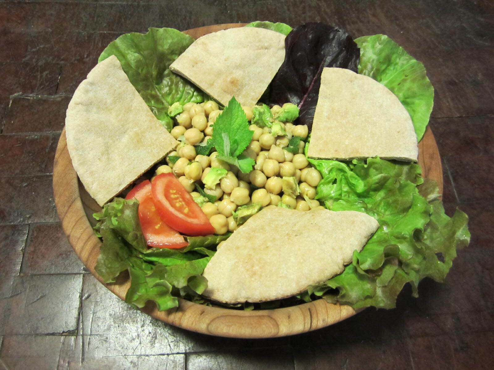 Bed of lettuce with chickpeas, sliced tomato, and pita bread